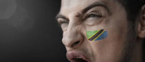 Ένας άντρας που ουρλιάζει με την εικόνα της εθνικής σημαίας της Τανζανίας στο πρόσωπό του. — Φωτογραφία Αρχείου