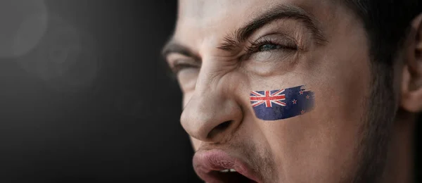 Um homem gritando com a imagem da bandeira nacional da Nova Zelândia em seu rosto — Fotografia de Stock