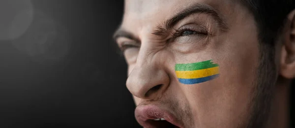 Křičící muž s obrazem Gabonské národní vlajky na tváři — Stock fotografie