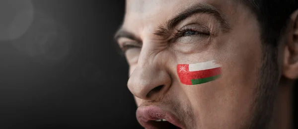 Um homem gritando com a imagem da bandeira nacional de Omã em seu rosto — Fotografia de Stock