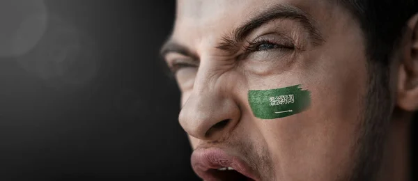 Ένας άντρας που ουρλιάζει με την εικόνα της εθνικής σημαίας της Σαουδικής Αραβίας στο πρόσωπό του. — Φωτογραφία Αρχείου