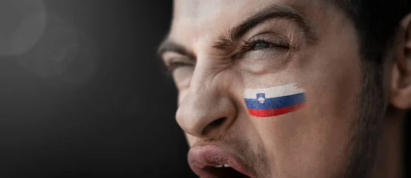 A screaming man with the image of the Slovenia national flag on his face — Stock Photo, Image