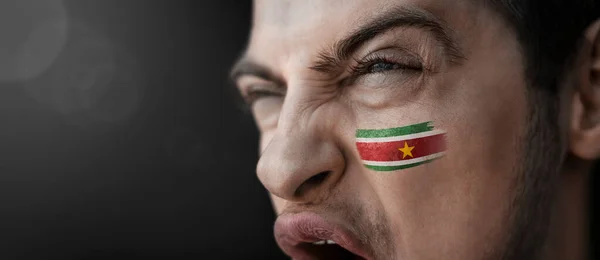 En skrikande man med bilden av Surinams flagga i ansiktet. — Stockfoto