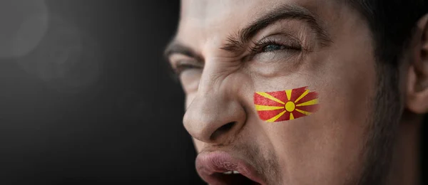 Un hombre gritando con la imagen de la bandera nacional de Macedonia en su cara — Foto de Stock