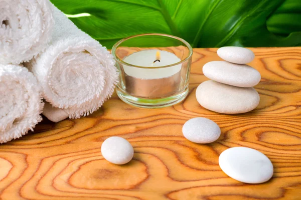 beautiful spa concept of white stones, candle, rolled towels and big green leaf on root wood background, close up