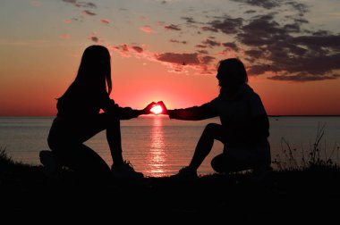 Deniz kıyısındaki iki kızın siluetleri. İki kız bir kalp gösterir. Günbatımında aşk.