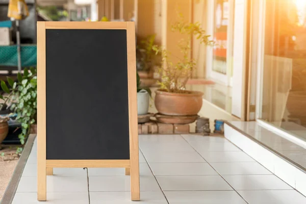 Wooden rustic blackboard in front of restaurant entrance. Mock up Menu Blank Blackboard sign stand Shop Cafe Restaurant. Street Magnetic Sidewalk Chalkboard.