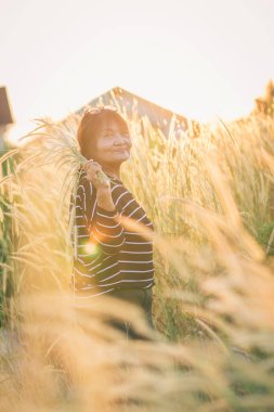 Yaşlı bir kadın yazın çim tarlasında kolları açık durur. Gün batımında kollarını kaldırmış bir kadın..