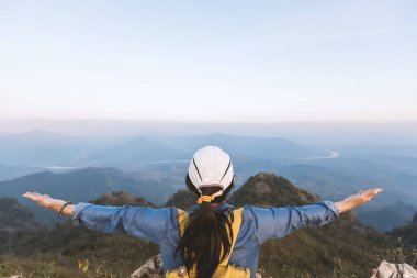 Yürüyüş yapan kadın ellerini kaldırdı ve zirveye ulaştı. Kız güneşe hoş geldin der. Kavramsal tasarım. Başarılı kadın yürüyüşçü, güneşin doğuşundaki dağın zirvesinde kollarını aç..