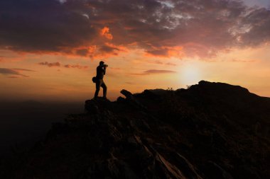 Siluet Adam fotoğrafçısı dağlarda dijital kamerayla fotoğraf çekiyor..