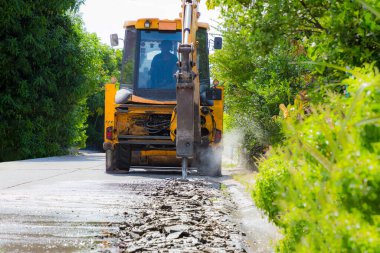 Kazıcı tamir için beton yolu kırıyor ve deliyor. İnşaat malzemelerinin hidrolik koluna monte edilmiş büyük bir pnömatik çekiç. İnşaat araçları yolu onarıyor. matkap matkabı