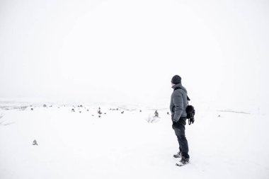 Genç adam karın üzerinde duruyor ve doğayı izliyor. Bir adamla kar tarlası. Genç adam karda tek başına duruyor ve uzaklara bakıyor. Beyaz, soğuk, karlı kış günü.