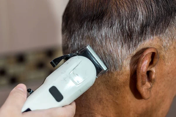 Old man having a hair cut by hairstylist using electrical battalion. men\'s hairstyling and hair cutting with hair clipper in a barber shop or hair salon