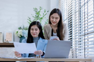 Ortaklardan oluşan bir grup Asyalı iş kadını dizüstü bilgisayarla ofiste projeyi tartışıyor. Profesyonel iş adamlarının iki meslektaşı birlikte çalışıyor..