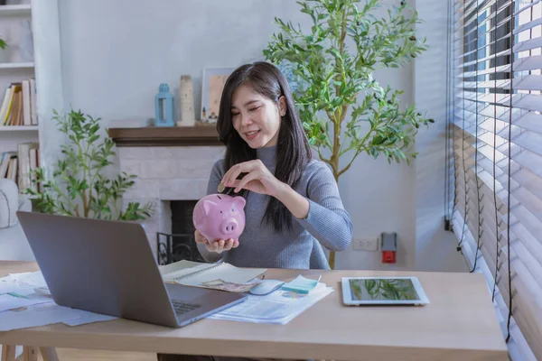 Kadın ev konseptinden çalışıyor. Muhasebe için para biriktiriyor. Tasarruf parası zenginlik kavramı, Asyalı iş kadını el yazısı yönetim bütçesi tasarruf maliyeti, nakit finans