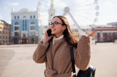 Açık hava video konferansı. Güzel bir kadının portresi. Genç bir kadın telefonda konuşuyor, şehir merkezinde caddede duruyor..