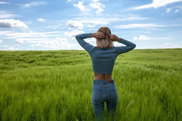 Sırt üstü uzanmış, kollarını açmış bir kadın. Buğday tarlasının ortasında genç bir kadın. Mavi gökyüzü. Mutluluk doğası yaz tatili ve insanlar arkada dans eden genç kadın konsepti.