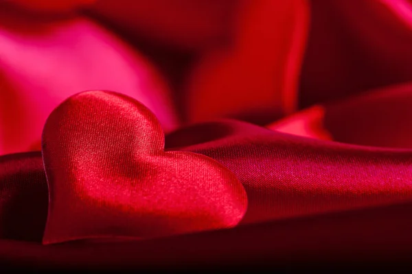 Červené srdce Valentýna symboly na červené hedvábné pozadí zblízka — Stock fotografie