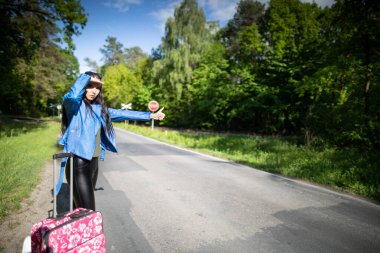 Bir genç elinde pembe bavuluyla ayakta duruyor ve tatile daha hızlı gitme fırsatını engellemeye çalışıyor..