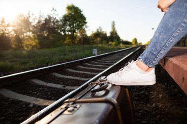 Eski bavul platformdaki rayların hemen yanında duruyor ve üzerinde de genç gezginin spor ayakkabıları var..