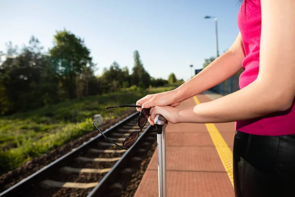 Una joven descansa las manos sobre el asa de la maleta y lleva gafas de sol en la mano. Viaja en tren cada fin de semana o más de vacaciones. —  Fotos de Stock