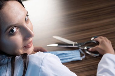 Genç bir tıp doktoru maskesinde oturuyor ve koruyucu maskeyi kesmeye hazırlanıyor. Böylece toplum üzerindeki süregelen salgın ve katı kısıtlamalar sona eriyor..