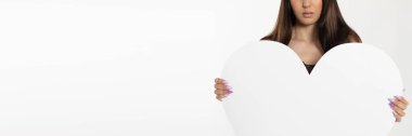 Genç bir kadın önünde kocaman beyaz bir kalp tutuyor. Açık ten rengi. Kalp şeklinde. Panoramik çerçeve.