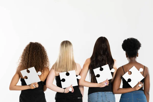 Four young girls of mixed ethnicity hold puzzles in their hands behind their backs with their backs to the camera. — Stock Photo, Image