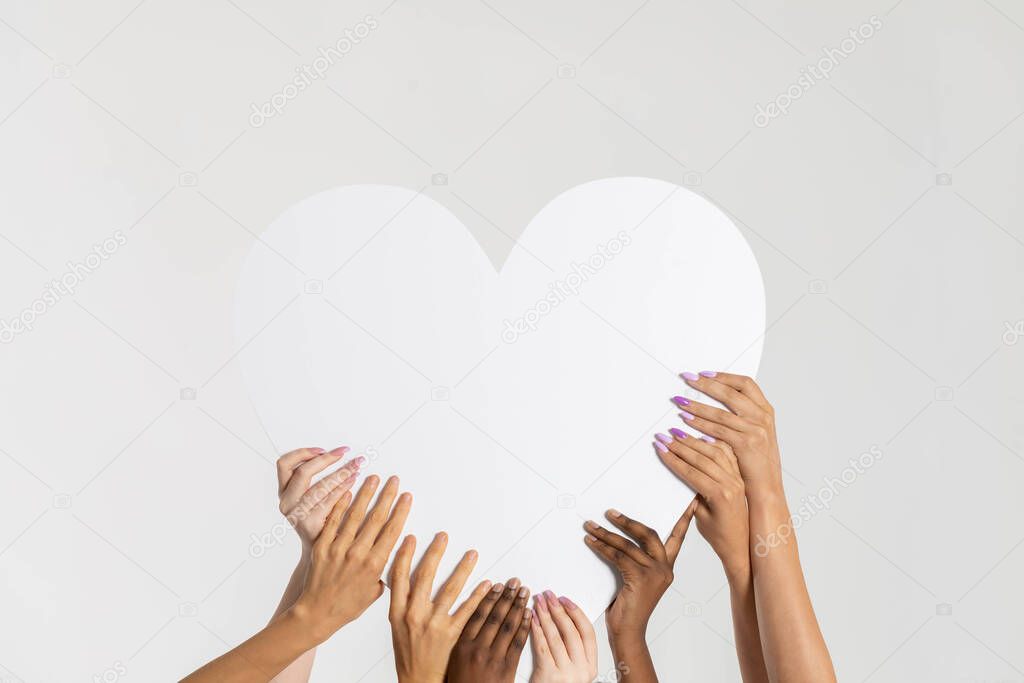 A large white heart held up by eight colored hands of different nations and races. Many races but a common pure heart.