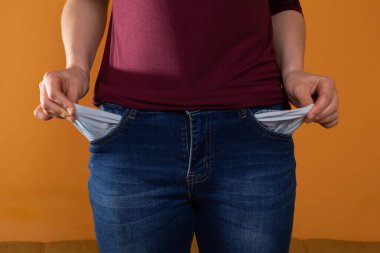Empty pockets in blue jeans are shown by a young woman while facing the lens. Pulls pockets out. Lack of money.
