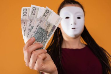 Anonim bir kadın, elinde yüz Polonyalı zloti değerinde kağıt banknotlarla elini uzatıyor. Yüzü yok çünkü üzerinde maske var..