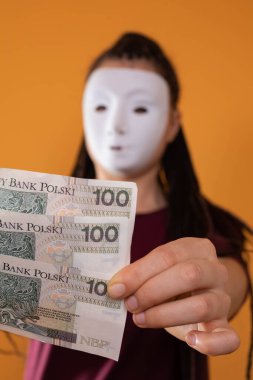 Anonim bir kadın, elinde yüz Polonyalı zloti değerinde kağıt banknotlarla elini uzatıyor. Yüzü yok çünkü üzerinde maske var..