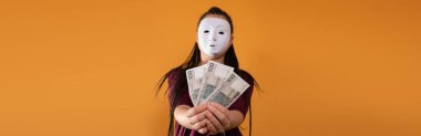 Panoramik bir çerçevede, isimsiz bir kadın elinde 100 Polonyalı zloti banknotuyla duruyor ve çiziyor. Yüzü yok çünkü üzerinde maske var..