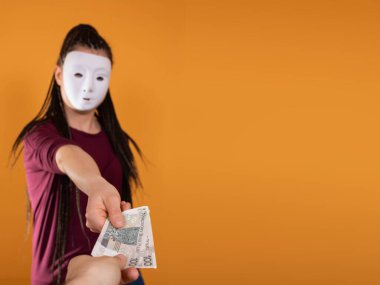 Anonim bir kadın, elinde yüz Polonyalı zloti değerinde kağıt banknotlarla elini uzatıyor. Yüzü yok çünkü üzerinde maske var..