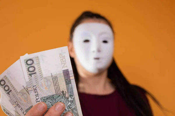 Una mujer anónima se para y tira de su mano con billetes de papel con el valor facial de cien zlotys polacos. No tiene cara porque tiene una máscara.. — Foto de Stock