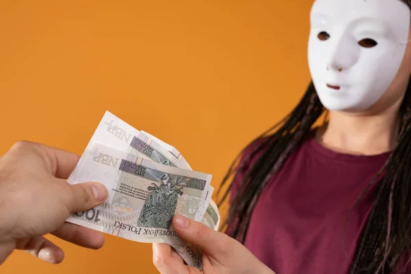 匿名の若い女性によって与えられた紙幣のための男性の手に達する。固体オレンジ色の孤立した姿. — ストック写真