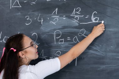 Genç bir kız, beyaz tebeşirle okul tahtasına yazı yazarak okuldaki matematik problemini çözüyor. Saçları iki at kuyruklu pembe bir kurdeleyle tutturulmuş..