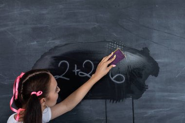 Ayakta duran bir genç, kirli bir okul tahtasını ıslak bir süngerle siliyor. Okul tahtası beyaz bir tuğla duvarda asılı. Yararlı bir kız tahtada duruyor..