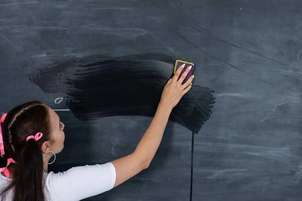 Un adolescent debout essuie un tableau noir sale de l'école avec une éponge humide. Le tableau noir de l'école est accroché à un mur de briques blanches. Une fille serviable se tient au tableau noir. — Photo