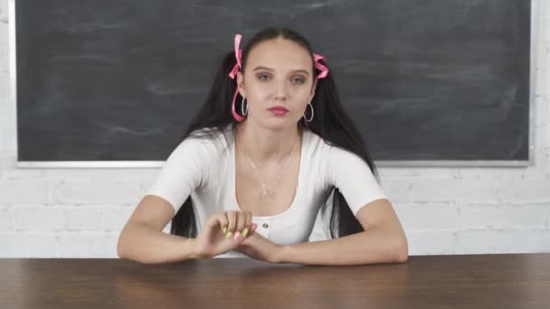 During school lessons, the student improves her hair and her image. Her hair is pinned with a pink ribbon in two ponytails. Teenager at the school desk. — Stock Video