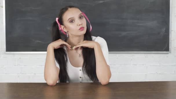 Κατά τη διάρκεια των μαθημάτων, η μαθήτρια βελτιώνει τα μαλλιά της και την εικόνα της. Τα μαλλιά της είναι καρφωμένα με ροζ κορδέλα σε δύο αλογοουρές. Έφηβος στο γραφείο του σχολείου. — Αρχείο Βίντεο