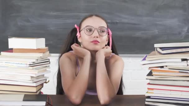 Een verveelde jonge tiener zit aan een schoolbureau tussen de stapels boeken en verveelt zich te wachten tot de volgende schoolles begint. — Stockvideo