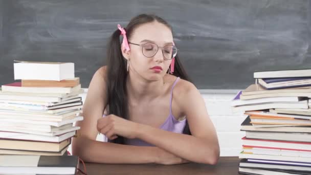 Sıkılmış bir genç okul masasında kitap yığınlarının arasında oturur ve bir sonraki dersin başlamasını beklemekten sıkılır.. — Stok video