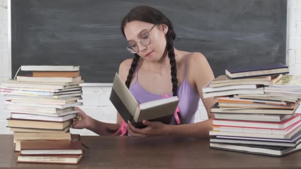I skolbiblioteket valde tonåringen ut en av de många böckerna och började läsa den. Bunden långt mörkt hår. Intresserad av läsning. — Stockvideo