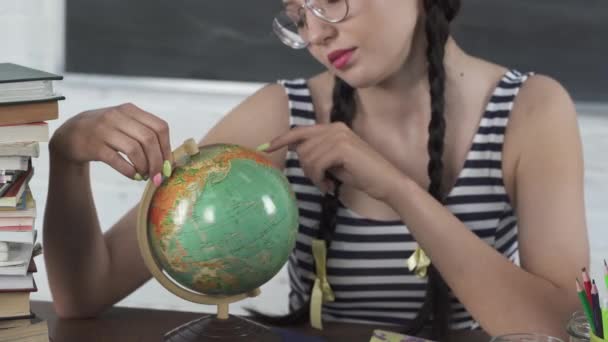 Урок географії. Підліток дивиться на земну кулю і шукає місце, де вона хотіла б піти на наступну відпустку і відпочити від навчання . — стокове відео