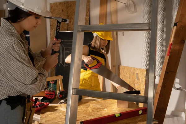 Las chicas trabajan con herramientas de carpintería. Una chica rubia corta una viga de madera y golpea con un martillo. — Foto de Stock