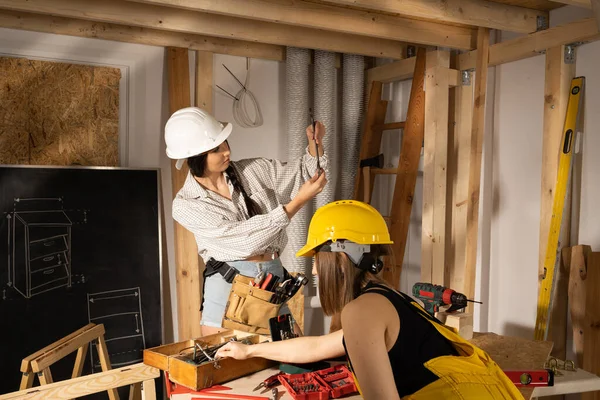 Las chicas están buscando las herramientas adecuadas en una caja llena de todo tipo de llaves de metal. El moreno y la rubia sonríen. — Foto de Stock