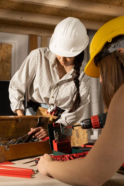 Las chicas están buscando las herramientas adecuadas en una caja llena de todo tipo de llaves de metal. El moreno y la rubia sonríen. — Foto de Stock