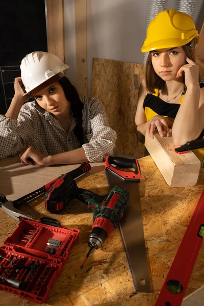 Dos chicas con ropa de trabajo están sentadas cansadas después de trabajar duro en un sitio de construcción. Chicas rubias y de cabello oscuro en el sitio de construcción. — Foto de Stock