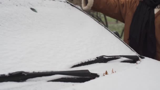 Una niña está paleando nieve del parabrisas del coche con un triángulo rojo plástico especial. La primera nieve en Lublin. — Vídeo de stock